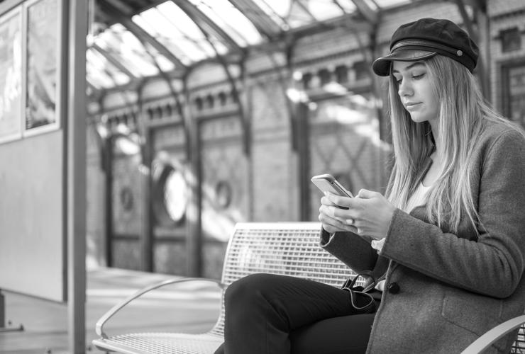 Woman on bench at train station looks at her phone